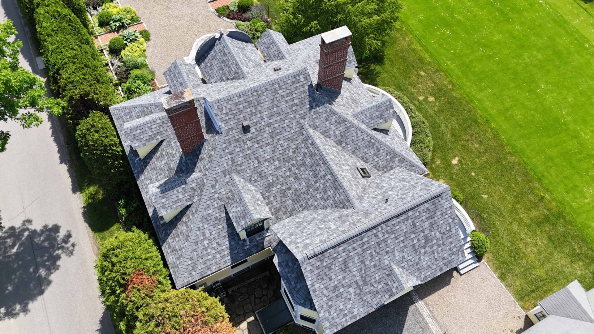 Aerial view of multi-level apartment complex with grey asphalt roof. Stone walkways lead to entrances, and shrubbery lines the sides.