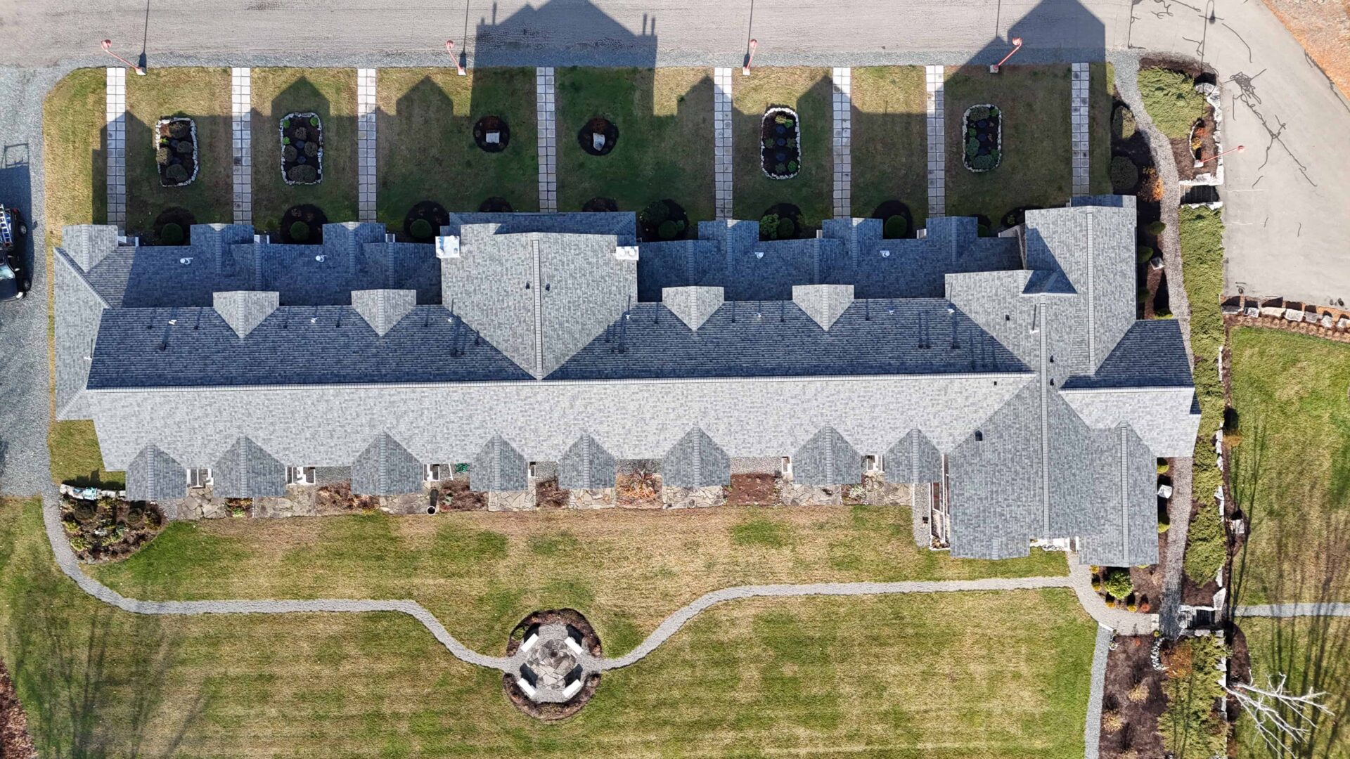 Aerial view of multi-level apartment complex with grey asphalt roof. Stone walkways lead to entrances, and shrubbery lines the sides.